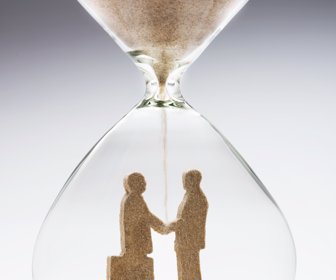 Two businessmen shaking hands made out of falling sand inside hourglass