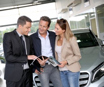 Couple in car dealership looking at brochure with salesman