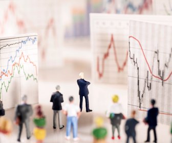 Banker stands on a pedestal of coins and looks at boards with different charts.