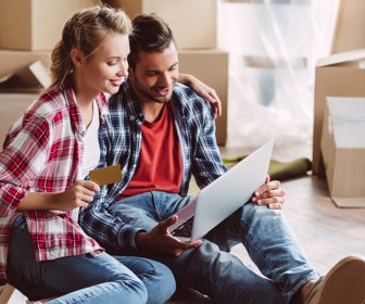 cheerful young couple using laptop and credit card in new apartment