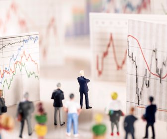 Banker stands on a pedestal of coins and looks at boards with different charts.
