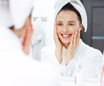 Young woman in bathrobe looking in bathroom mirror