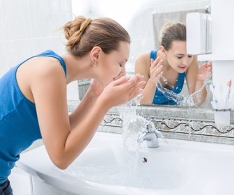 Young woman washing her face with clean water in bathroom